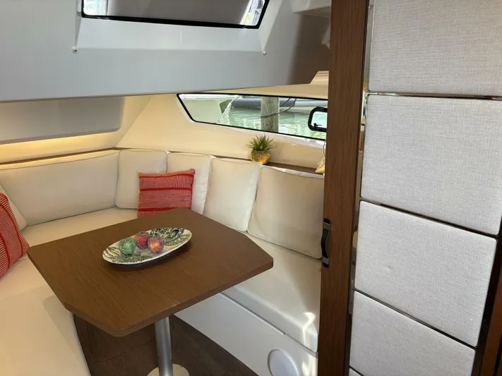 Jeanneau Yacht Photos Pics 2024 Jeanneau 12.5 Walk interior with cozy seating, wooden table, and decorative pillows.