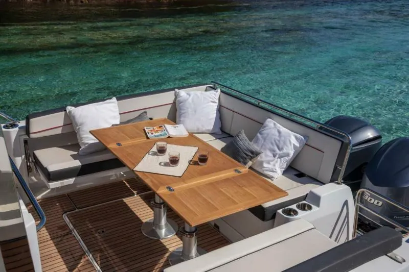  Yacht Photos Pics Luxurious Jeanneau 10.5 WALK 2024 boat interior with wooden table and cushions by clear water.
