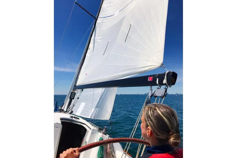 Targa Yacht Photos Pics Person steering 2008 Beneteau First 10R sailboat on open water under clear blue sky.