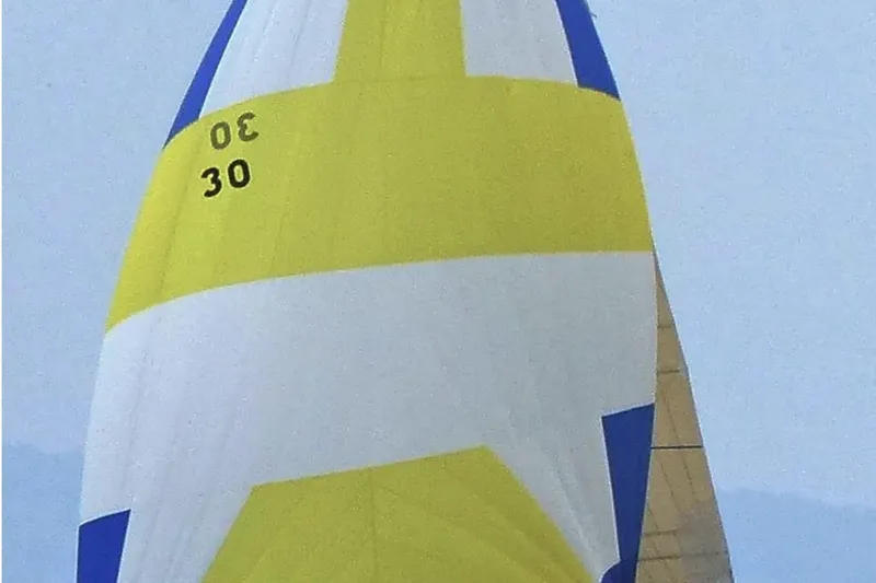 Targa Yacht Photos Pics Yellow and blue sail of a 2008 Beneteau First 10R yacht against a clear sky.