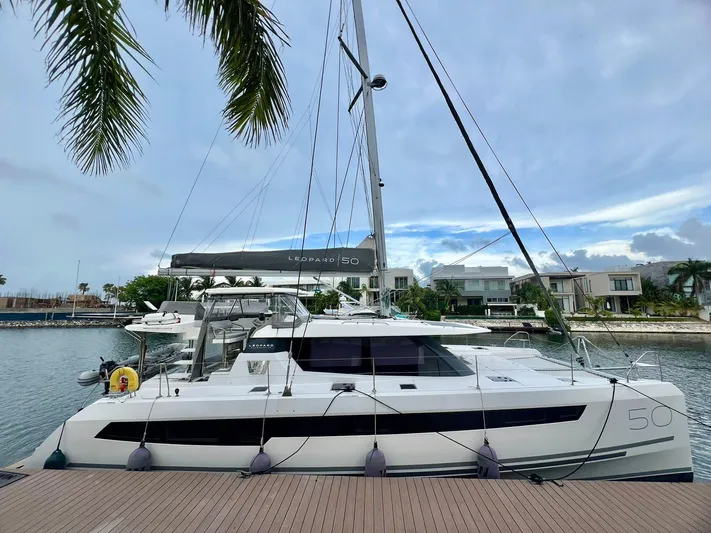 Win Win Yacht Photos Pics 2022 Leopard 50 catamaran docked at marina, surrounded by palm trees and waterfront homes.