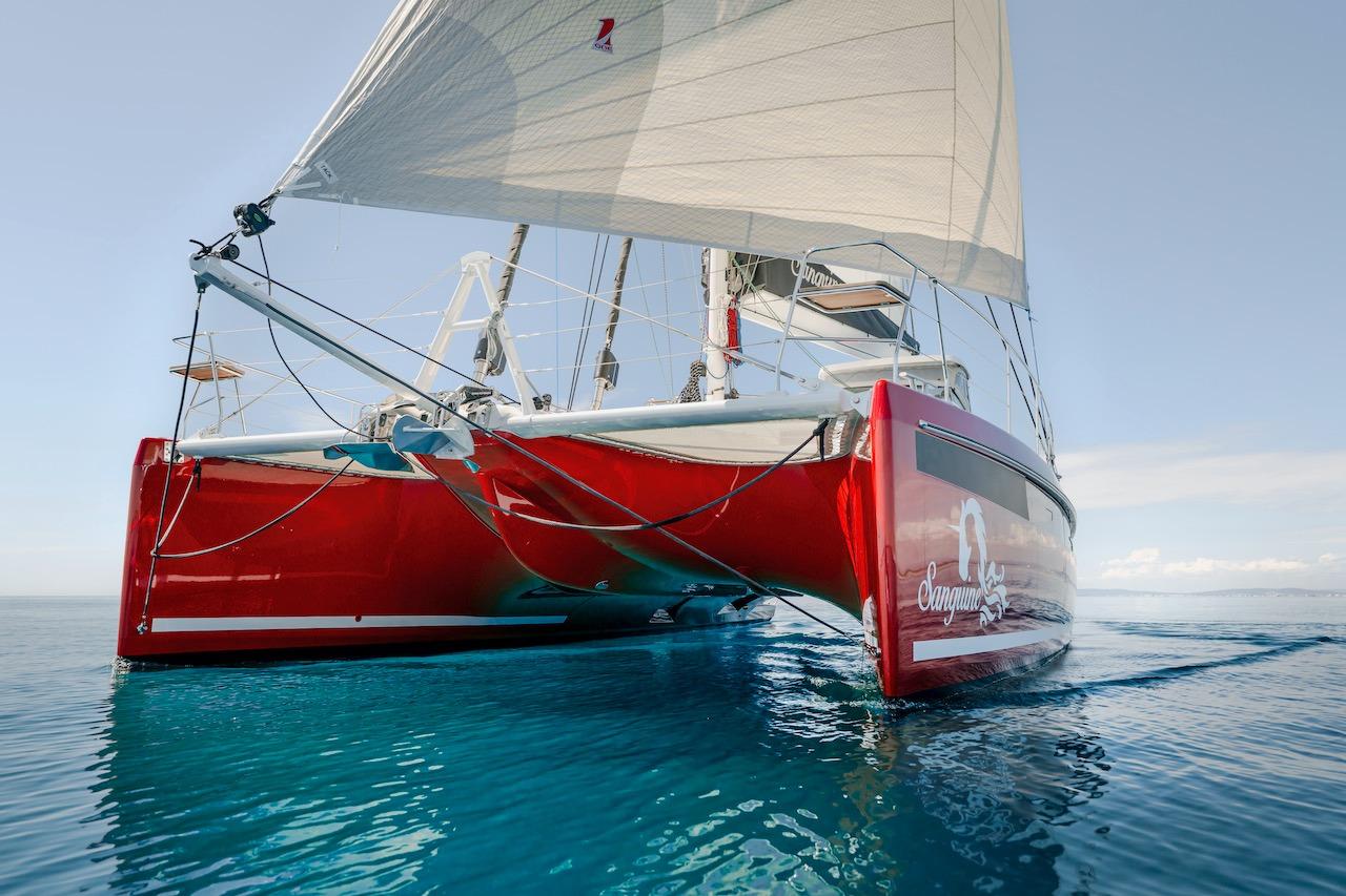 Red Privilege Signature 510 catamaran sailing on clear water, year 2025.