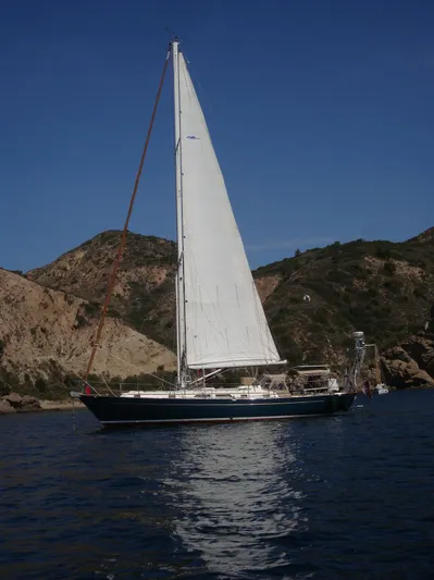 Joy Yacht Photos Pics Sailboat "Passport Royal 43" from 1999 on calm water with rocky hills in the background.