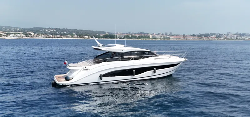  Yacht Photos Pics 2024 Princess V55 yacht cruising on calm blue waters near a coastal city.