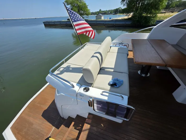  Yacht Photos Pics 2019 Sunseeker Predator 50 yacht deck with seating, table, and American flag by the water.