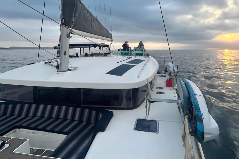  Yacht Photos Pics 2018 Lagoon 450 S catamaran sailing at sunset with passengers on deck.