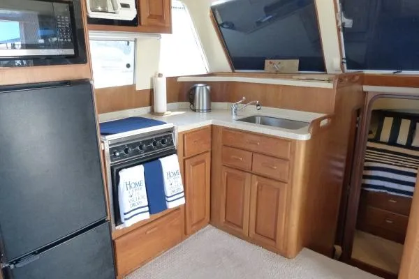  Yacht Photos Pics 1999 Mainship 350 Trawler kitchen with wood cabinetry, appliances, and cozy sleeping area.