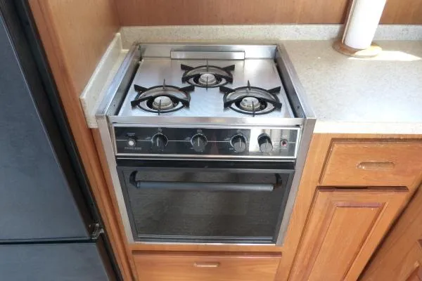  Yacht Photos Pics 1999 Mainship 350 Trawler kitchen with a three-burner stove and oven, wooden cabinetry.