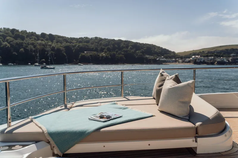 Chase Yacht Photos Pics Luxurious 2023 Princess X80 yacht deck with cushions, overlooking serene water and lush landscape.
