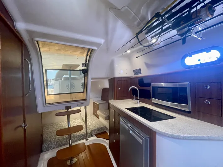 Hobi One Yacht Photos Pics 2015 Pursuit 345 Offshore cabin interior with kitchenette, seating, and fishing rod storage.