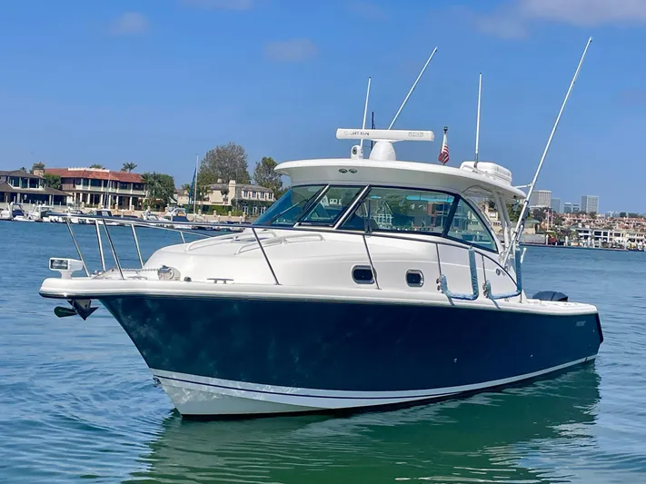 Hobi One Yacht Photos Pics 2015 Pursuit 345 Offshore boat on calm water, with coastal buildings in the background.