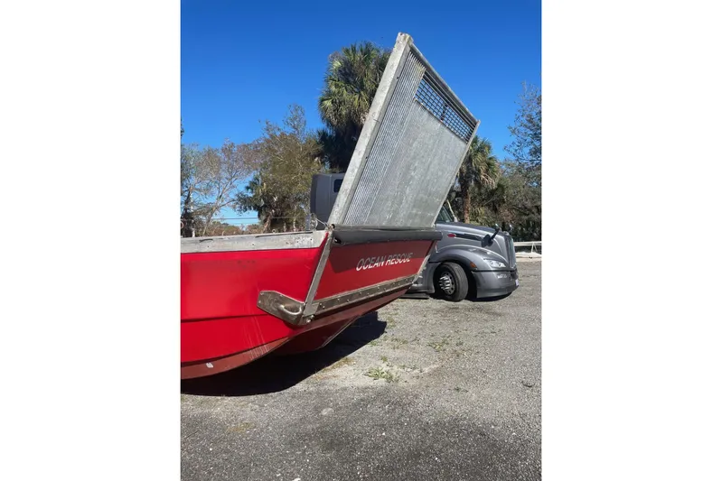 Asi Tender Yacht Photos Pics Red 1987 Commercial Buoy Tender with open ramp, parked near a truck, surrounded by trees.