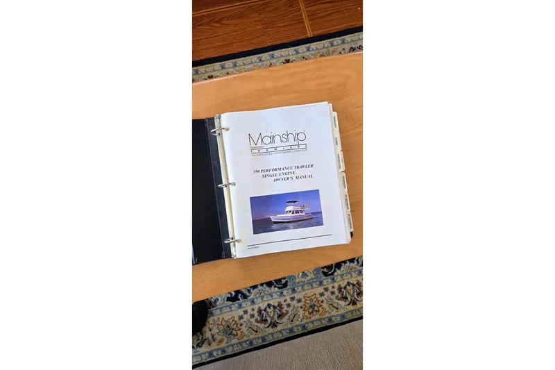 Polly Yacht Photos Pics Manual for 2000 Mainship 390 Trawler on wooden table, open binder view.