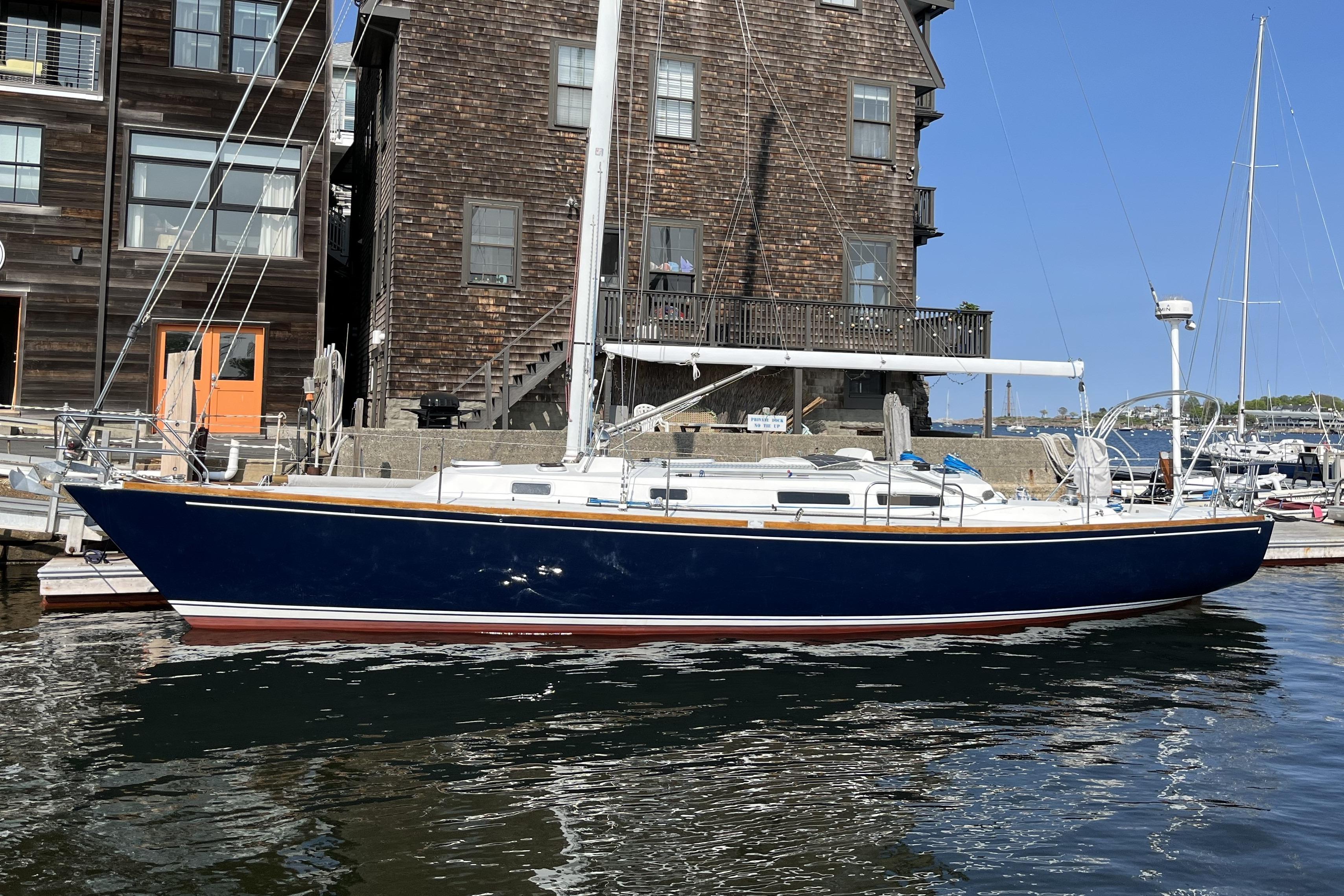1997 J Boats J/42 sailboat docked by rustic building, clear blue sky.