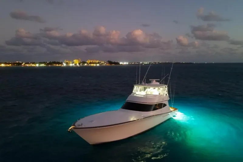 Boujie Yacht Photos Pics 2025 Viking 82 Convertible yacht illuminated on calm ocean at dusk, city lights in background.