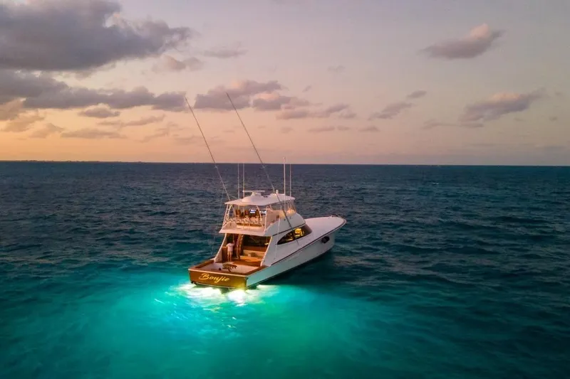 Boujie Yacht Photos Pics 2025 Viking 82 Convertible yacht illuminated on ocean at sunset.