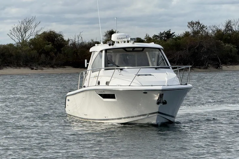  Yacht Photos Pics 2017 Pursuit OS 325 Offshore boat cruising on water near a wooded shoreline.