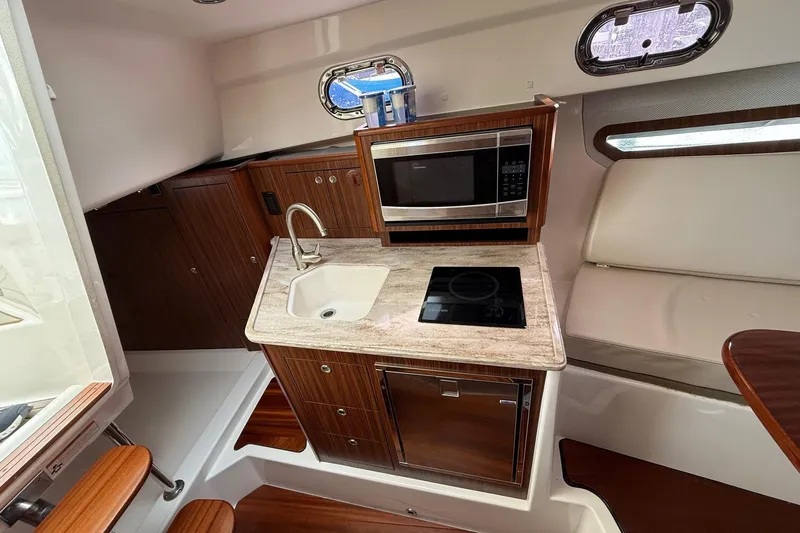 Yacht Photos Pics 2017 Pursuit OS 325 Offshore boat interior with kitchenette, featuring sink, stove, and microwave.