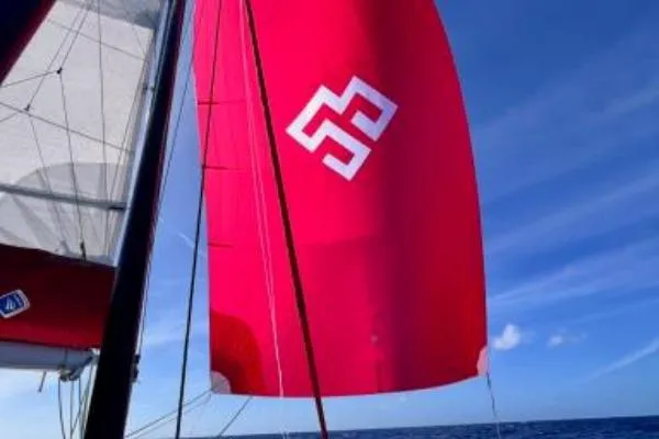 Meraki Yacht Photos Pics Red sail of 2022 NEEL 43 trimaran against clear blue sky.