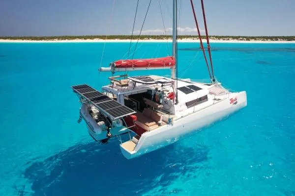 Meraki Yacht Photos Pics 2022 NEEL 43 trimaran sailing in clear turquoise waters near a sandy beach.