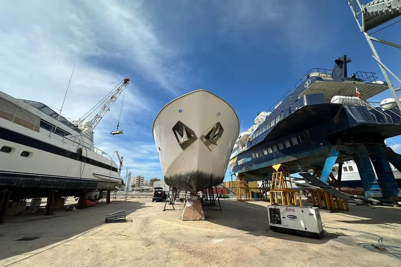  Yacht Photos Pics Sanlorenzo 82 yacht from 1998 in a shipyard, surrounded by cranes and other vessels.