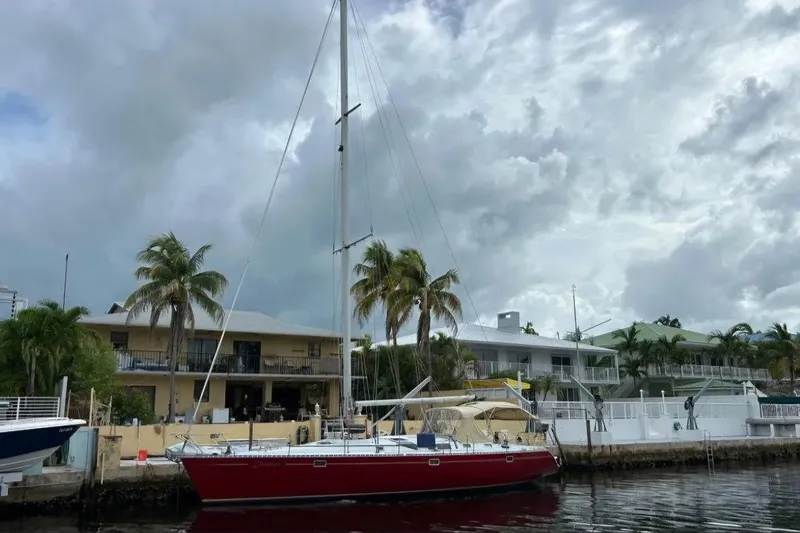 Zephyrus Yacht Photos Pics Red 1991 Beneteau Oceanis 50 sailboat docked near waterfront homes under cloudy sky.