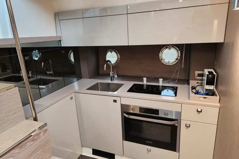  Yacht Photos Pics Modern kitchen interior of 2023 Cranchi M44 HT yacht with sleek appliances and porthole windows.