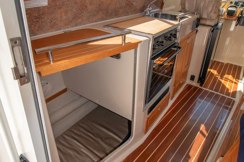 R Time Yacht Photos Pics 2013 Aspen C90 boat interior with compact kitchen, featuring stove, sink, and wooden cabinetry.