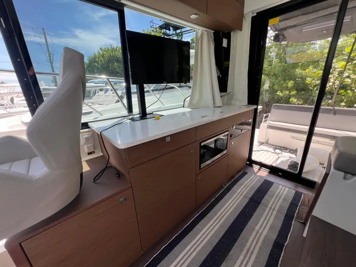  Yacht Photos Pics Interior of 2023 Jeanneau 1095 NC boat with modern seating, TV, and striped rug.