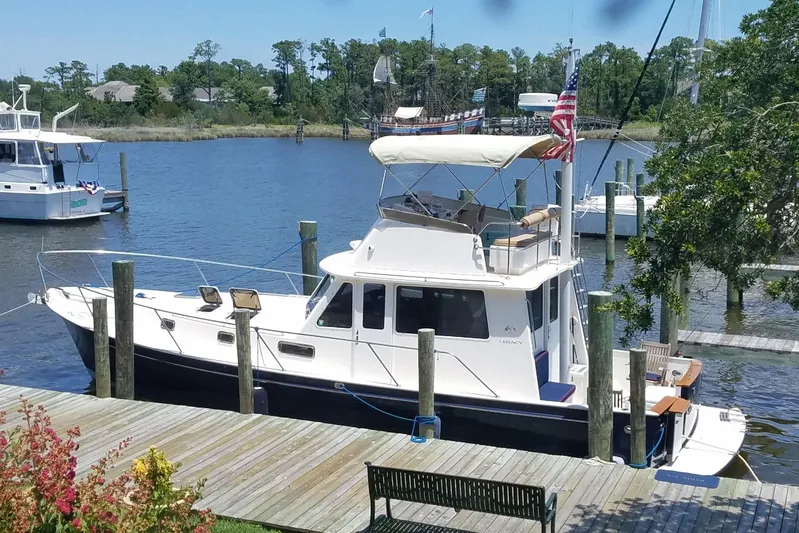 Escapade Yacht Photos Pics 1999 Legacy Yachts 40 Sedan docked by a scenic waterfront with trees and other boats.