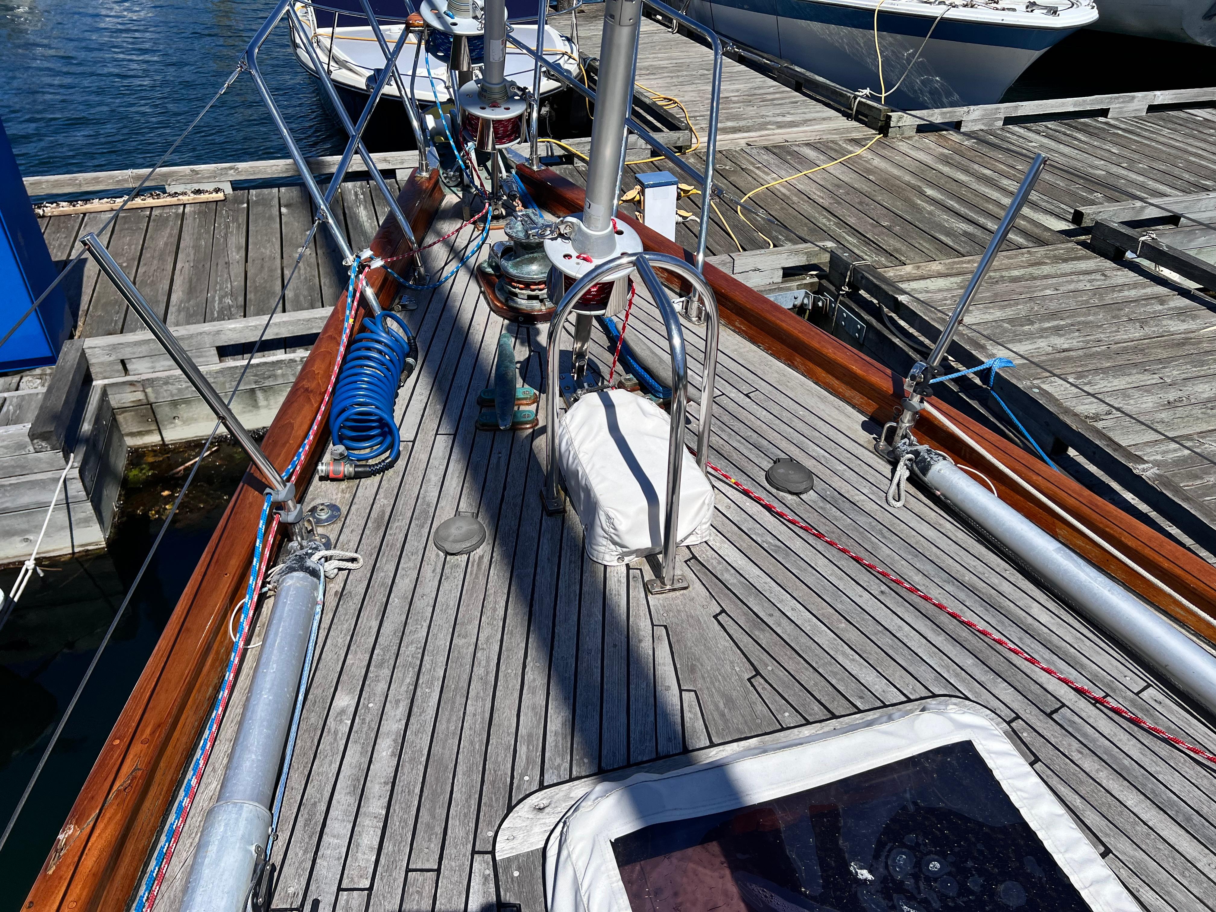 Sailboat deck of 1987 Reliance 45, docked at marina with wooden planks and nautical equipment.
