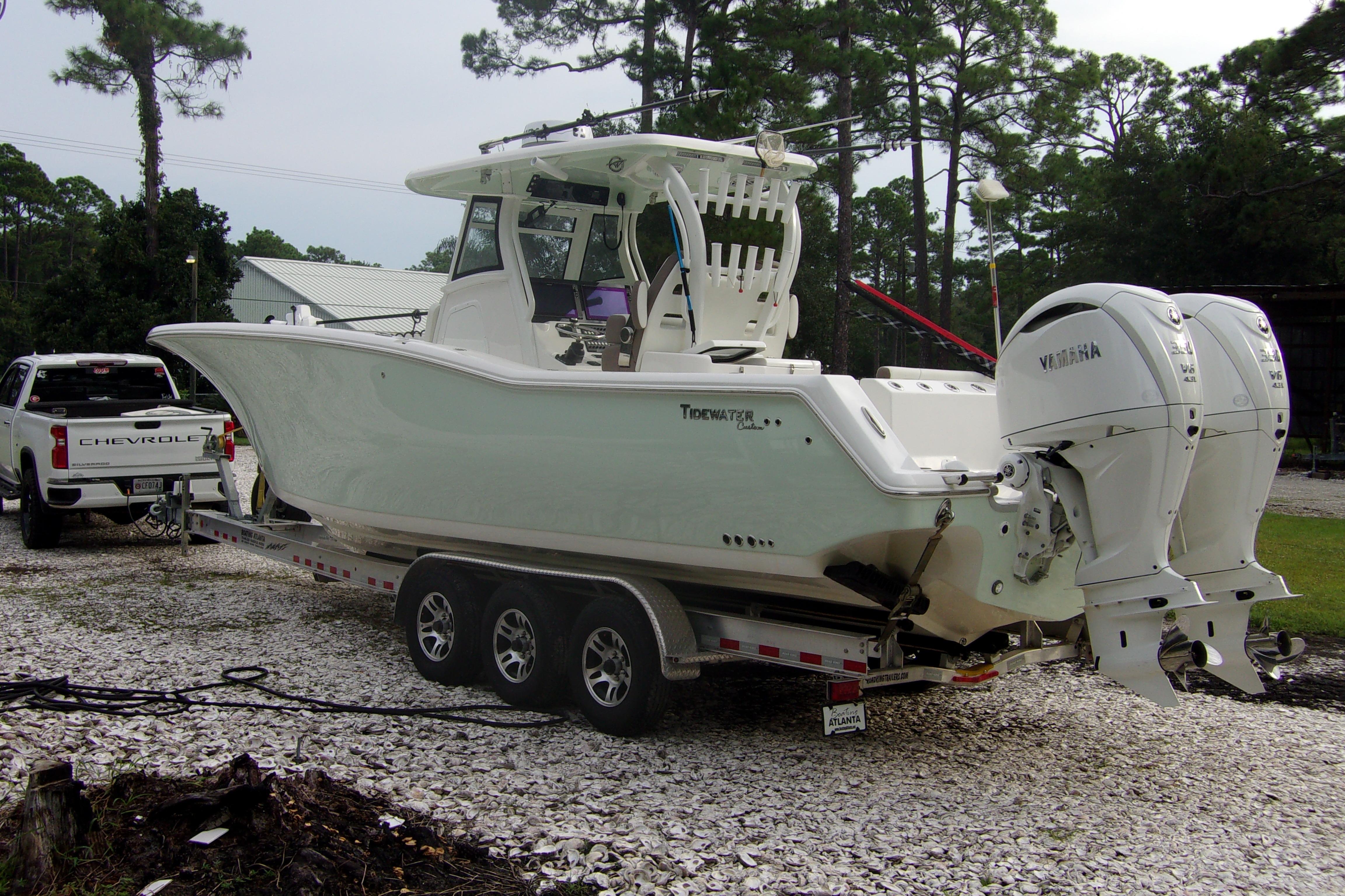 2025 Tidewater 320 CC Adventure boat on trailer, parked near trees and a Chevrolet truck.