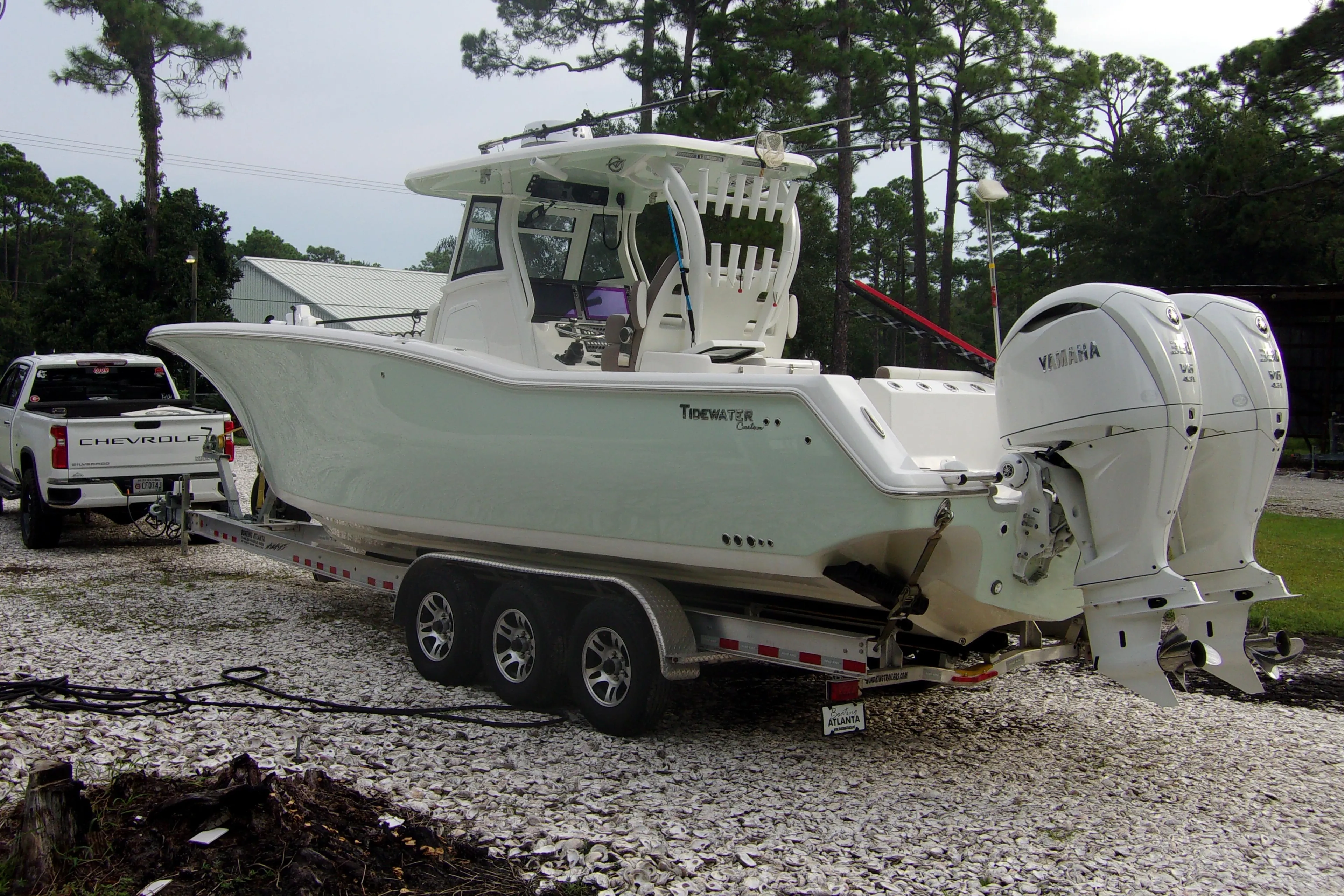 2025 Tidewater 320 CC Adventure boat on trailer, parked near trees and a Chevrolet truck.
