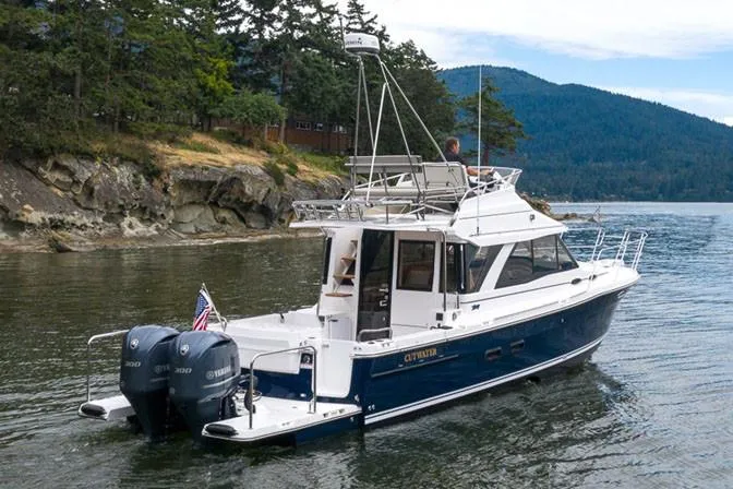  Yacht Photos Pics Manufacturer Provided Image: 2022 Cutwater C-32 CB boat cruising near a rocky shoreline with scenic forested hills.