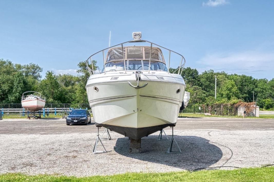 2002 Larson Cabrio 330 boat on stands, parked outdoors with trees in the background.