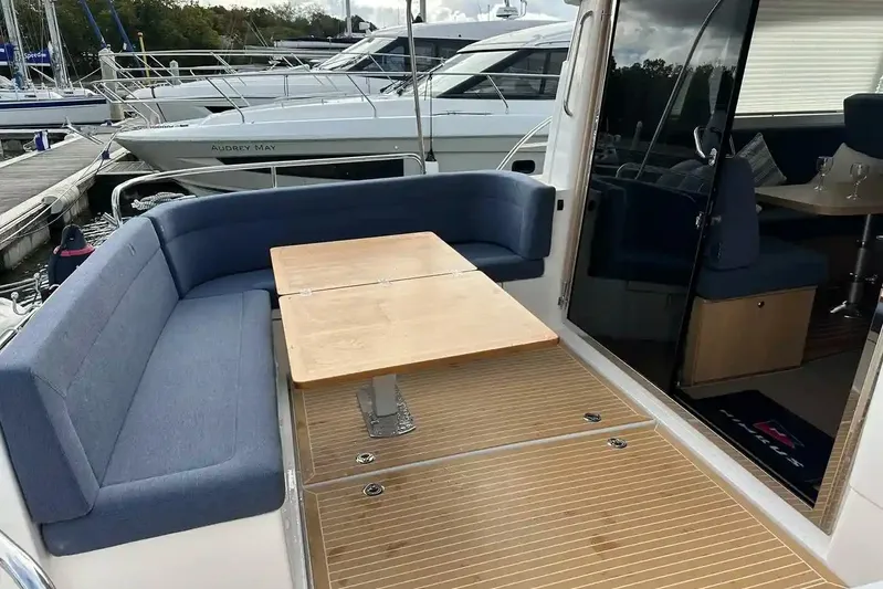 Bertie Yacht Photos Pics Outdoor seating area on 2024 Nimbus 405 Coupé yacht with wooden table and blue cushions.