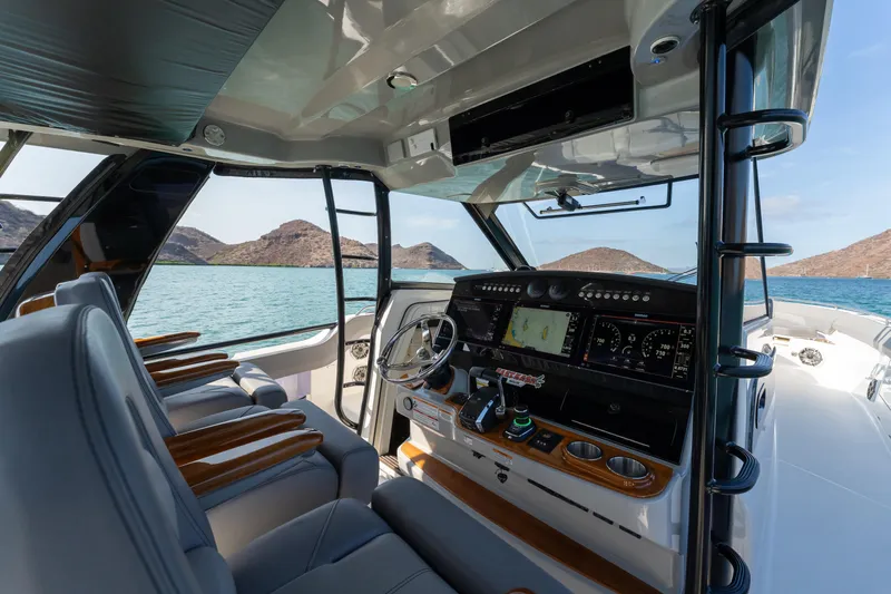 Fast Kash Yacht Photos Pics 2023 Boston Whaler 420 Outrage helm with advanced navigation, overlooking serene waters and distant hills.