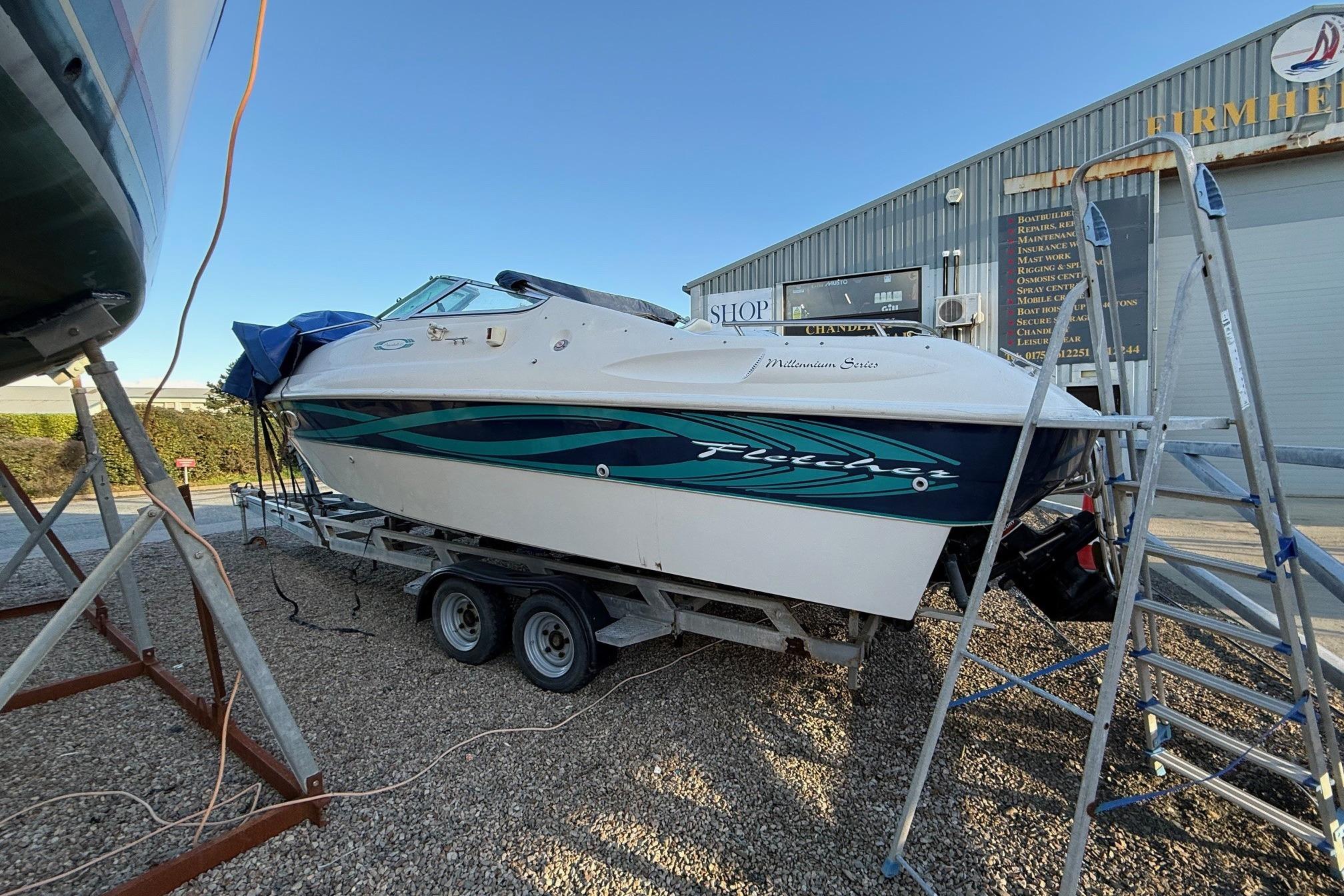 Fletcher Arrowbolt 25 boat from 2000 on trailer, parked near a marine shop.