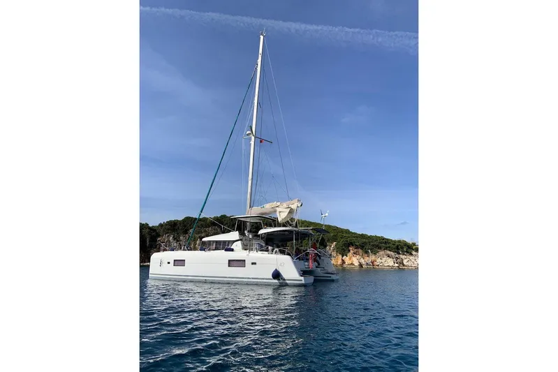  Yacht Photos Pics 2017 Lagoon 42 catamaran anchored in serene blue waters near a rocky shoreline.
