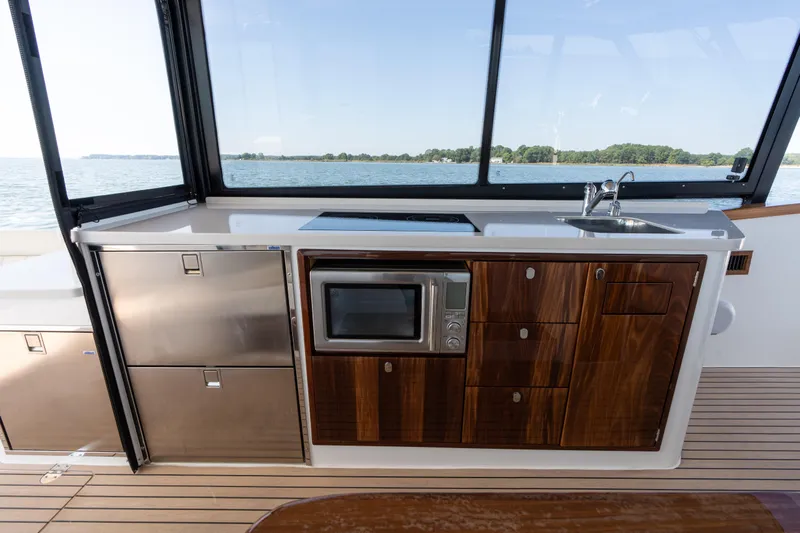 Middle Path Yacht Photos Pics Modern kitchen area on 2023 MJM Yachts 4, featuring wood cabinetry and stainless steel appliances.