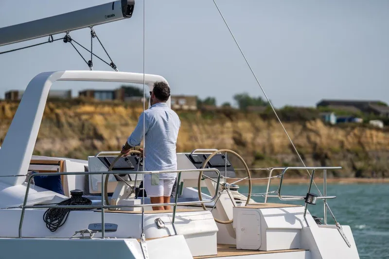 Off The Grid Yacht Photos Pics Man steering 2024 Southerly 420 sailboat near rocky coastline.