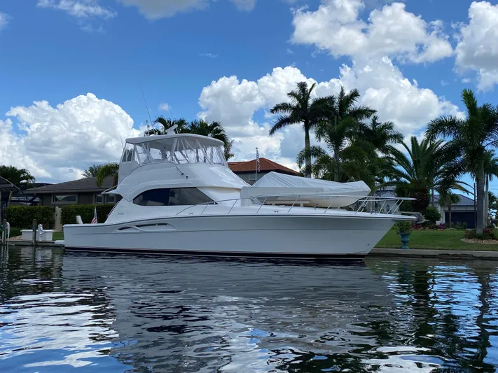 Pretty Fine Yacht Photos Pics 2003 Riviera 47 Convertible yacht docked by palm trees under a blue sky.
