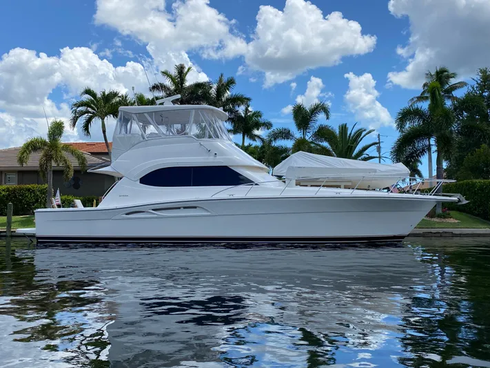 Pretty Fine Yacht Photos Pics 2003 Riviera 47 Convertible yacht docked by palm trees under a blue sky.