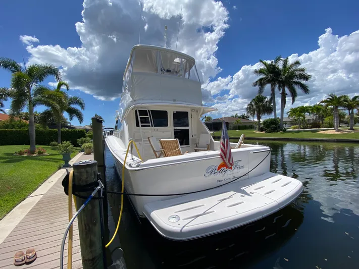 Pretty Fine Yacht Photos Pics 2003 Riviera 47 Convertible yacht docked by palm trees under a blue sky.
