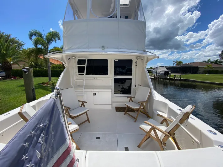 Pretty Fine Yacht Photos Pics 2003 Riviera 47 Convertible yacht deck with chairs and American flag, docked by a canal.