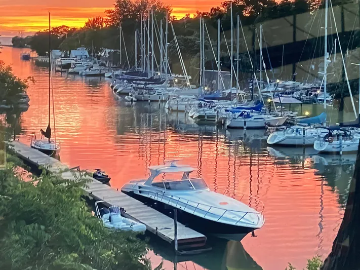 Dealer-ship Yacht Photos Pics 2004 Fountain 48 Express Cruiser docked at sunset, surrounded by sailboats and vibrant orange sky.