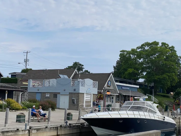 Dealer-ship Yacht Photos Pics 2004 Fountain 48 Express Cruiser docked near quaint waterfront buildings and trees.