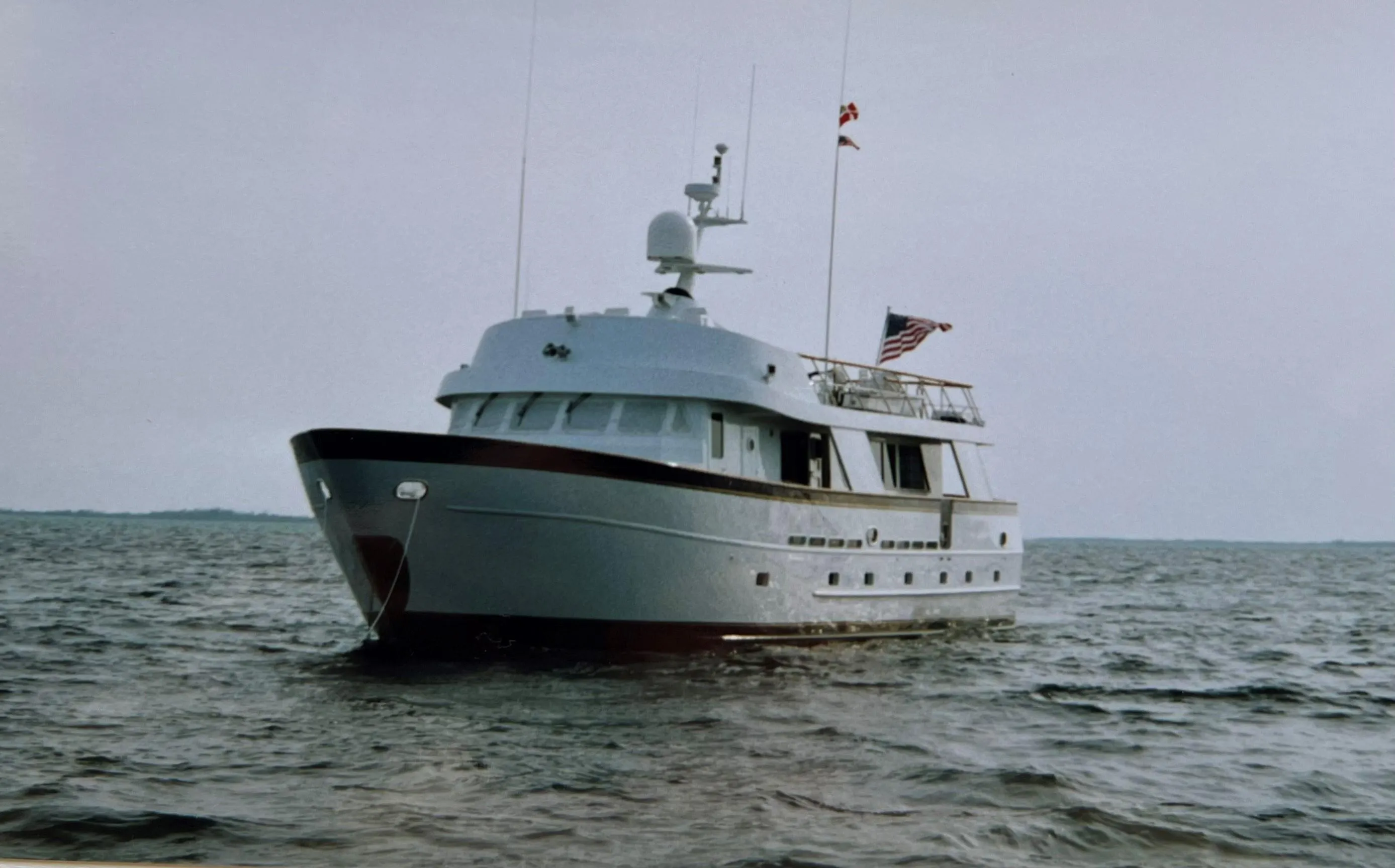 Custom 1988 steel motor yacht on open water, featuring sleek design and American flag.