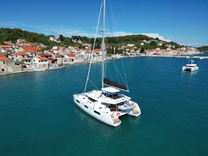Mare Azul Yacht Photos Pics 2024 Lagoon 46 catamaran sailing near a coastal village with red-roofed houses.