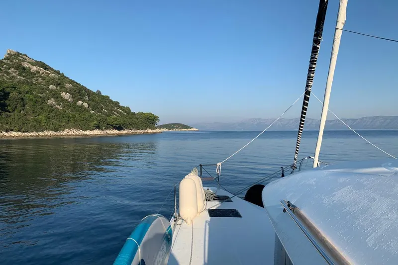 Twin Joy Yacht Photos Pics Lagoon 50 catamaran sailing near a scenic coastline, clear blue sky, and calm waters.